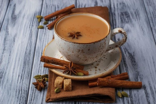 Chá indiano masala chai servido em xícara com canela, anis estrelado e especiarias ao redor