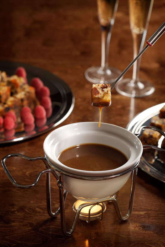 Fondue de chocolate servido em rechaud com frutas e pedaços de bolo mergulhados na calda
